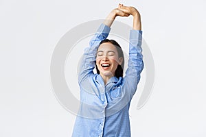 Smiling beautiful asian girl in pajamas stretching with satisfied face, yawning with closed eyes, had good sleep or nap
