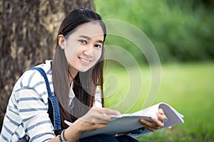 Smiling beautiful Asian girl reading book and working at tree on