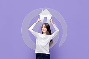 Smiling beautiful Asian woman holding house symbol overhead