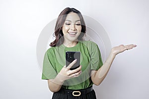 Smiling beautiful Asian woman pointing finger sideward to empty space while holding her phone isolated white background