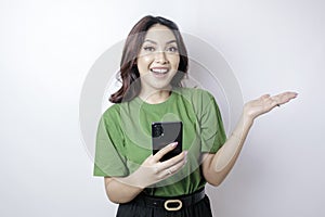 Smiling beautiful Asian woman pointing finger sideward to empty space while holding her phone isolated white background