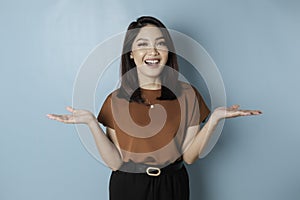 Smiling beautiful Asian woman pointing finger sideward to empty space isolated blue background