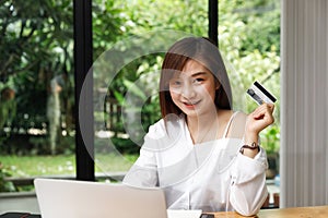 Smiling beautiful Asian woman presenting credit card in hand showing trust and confidence for making payment. Online shopping