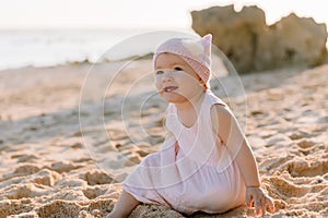 Smiling beautiful baby girl in outdoor with sunset. Happy child in pink dress on ocean beach