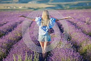 Smiling beautiful blond lady model on lavender field enjoy summer day wearing airy whit dress with bouquet of flowers