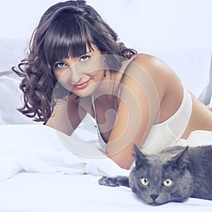 Smiling beautiful brunette girl in her bed and cat