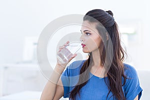 Smiling beautiful brunette sitting on the couch and drinking water