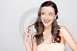 Smiling beautiful brunette woman with curls and makeup  on grey