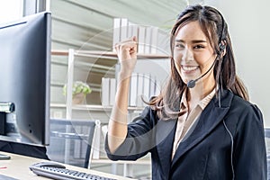 Smiling beautiful businesswoman with headset working in call center as a customer service agent celebrating a good job