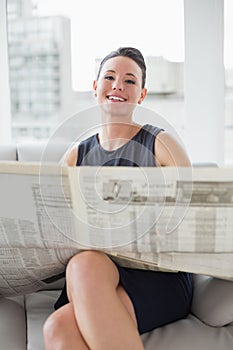 Smiling beautiful businesswoman reading newspaper on sofa