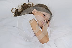 Smiling beautiful child girl lying on a pillow, white bed, close-up face