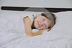 Smiling beautiful child girl lying on a pillow, white bed, close-up face