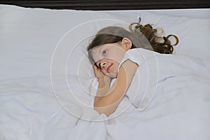 Smiling beautiful child girl lying on a pillow, white bed, close-up face