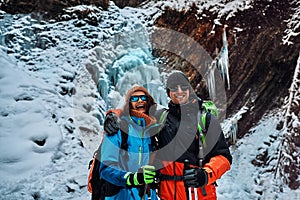 Smiling beautiful couple dressed in warm winter sportswear, sunglasses and gloves holding trekking poles, looking at the camera