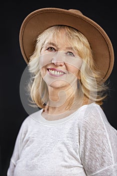 Smiling beautiful elderly blonde woman in a hat and white jacket. Active life and positivity in adulthood. Close-up. Black