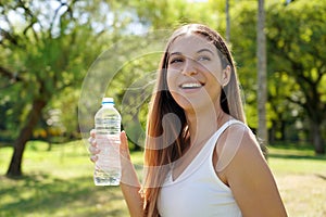 Smiling beautiful fitness woman have a break from work out holding a bottle of water to drink looking away in city park