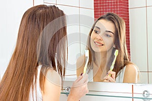 Smiling beautiful girl looks in the mirror and holding a toothbrush