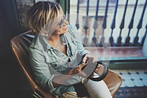 Smiling beautiful girl relaxing at home,playing music using smartphone and wearing sun glasses and modern headphones