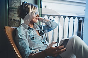 Smiling beautiful girl relaxing at home,playing music using smartphone and wearing sun glasses and modern headphones