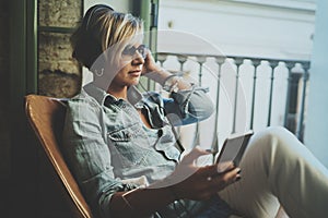 Smiling beautiful girl relaxing at home,playing music using smartphone and wearing sun glasses and modern headphones