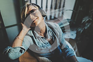 Smiling beautiful girl relaxing at home,playing music using smartphone and wearing sun glasses and modern headphones