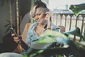 Smiling beautiful girl relaxing at home,wearing casual clothes,playing music,using smartphone and listening audio books