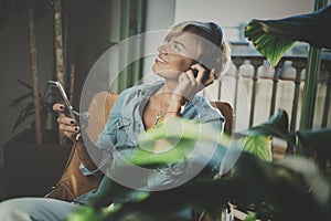 Smiling beautiful girl relaxing at home,wearing casual clothes,playing music,using smartphone and listening audio books