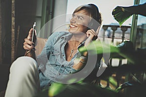 Smiling beautiful girl relaxing at home,wearing casual clothes,playing music,using smartphone and listening audio books