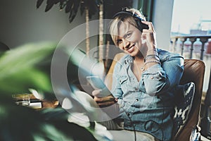 Smiling beautiful girl relaxing at home,wearing casual clothes,playing music,using smartphone and listening audio books