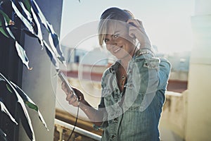 Smiling beautiful girl relaxing at home,wearing casual clothes,playing music,using smartphone and listening audio books