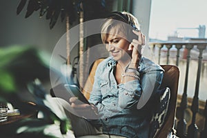 Smiling beautiful girl relaxing at home,wearing casual clothes,playing music,using smartphone and listening audio books