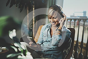 Smiling beautiful girl relaxing at home,wearing casual clothes,playing music,using smartphone and listening audio books