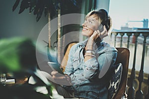 Smiling beautiful girl relaxing at home, wearing casual clothes, playing music, using smartphone and listening audio books