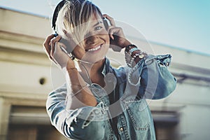 Smiling beautiful girl relaxing at home,wearing casual clothes,playing music,using smartphone and listening audio books