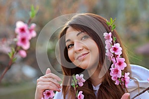 Smiling beautiful girl standing near a peach tree during sunset. Happy face. Spring time