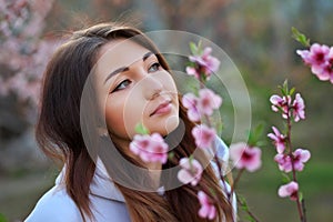 Smiling beautiful girl standing near a peach tree during sunset. Happy face. Spring time