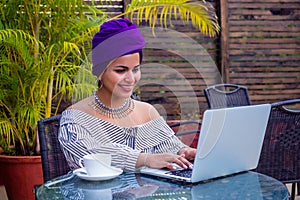 Smiling beautiful indian girl with ethnic turban on head culture working on laptop outdoors summer cafe