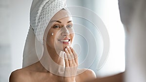 Smiling beautiful lady apply skincare cream look in mirror