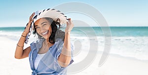 Smiling beautiful latin woman on beach with straw hat at sea