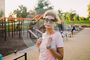 Smiling beautiful mature woman with skipping rope posing against backdrop of street gym after workout. Older woman with