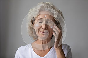 Smiling beautiful middle aged senior retired woman nourishing moisturizing face.