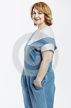 Smiling beautiful middle-aged woman with red hair in denim overalls and a white T-shirt. Activity and longevity. White background