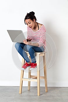 Smiling beautiful multi-ethnic girl sitting on stool with computer