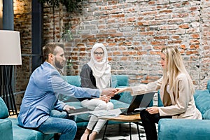 Smiling beautiful muslim businesswoman in hijab, working in modern office with her Caucasian male and female partners