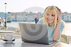 Smiling beautiful teenage girl in headphones looking into a laptop.