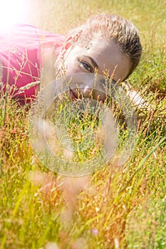Smiling beautiful teenage girl lying down, looking through the grass