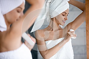 Smiling beautiful woman applying antiperspirant to armpit in bathroom
