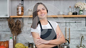 Smiling beautiful woman in apron posing with crossed hand at cosiness kitchen interior