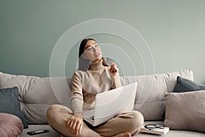 Smiling beautiful woman holding credit card and using laptop computer sitting on couch at home. Online shopping concept.
