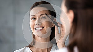 Smiling beautiful woman looking in mirror, applying mascara on lashes